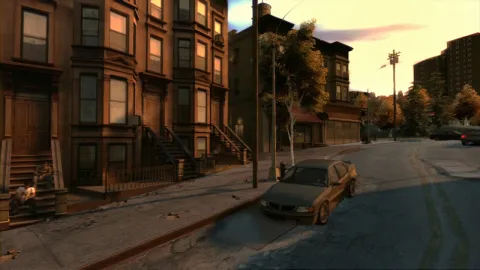 An old looking car drives down a worn street past some houses.