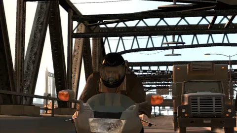 Niko rides a motorbike with a helmet on. A truck is see in in the background.