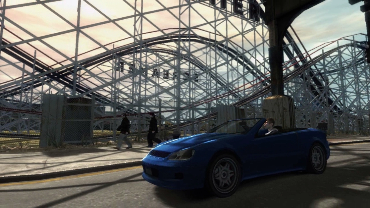 A blue sports car drives past a fairground.