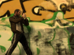 Niko walks along a grafitti covered wall, gun drawn.